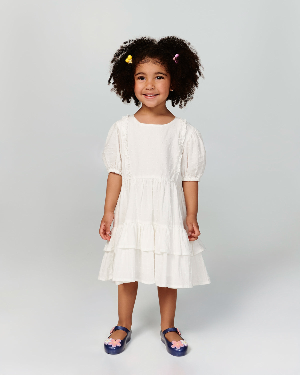 Child model in a white dress wearing a pair of metallic blue Sweet Love Picnic baby flats with flowers