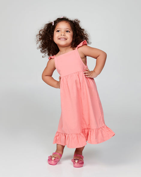 Child model in a coral dress wearing a pair of pink Ultragirl Princess baby ballerina flats.