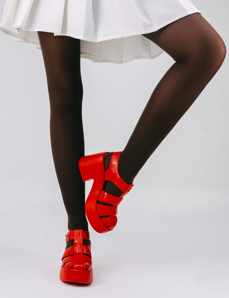 Model's legs in a white skirt and black tights wearing a pair of red Lulu platform sandals