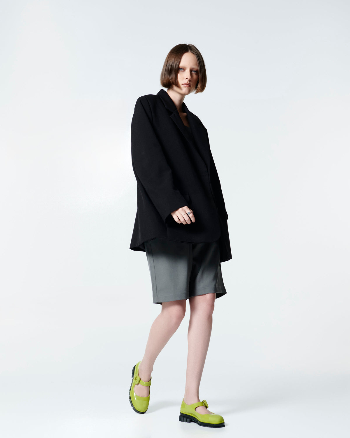 Model in grey skirt and black blazer wearing a pair of green with black sole June mary janes with matte toe cap