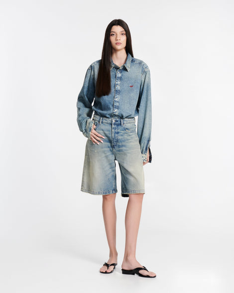 Model in jean shorts and jean button down shirt wearing a pair of black Flip Flop + Diesel sandals