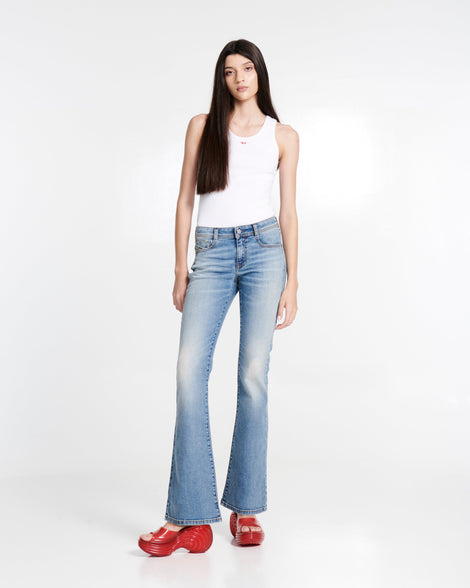 Model in jeans and a white tank top wearing a pair of transparent red Platforms + Diesel slides