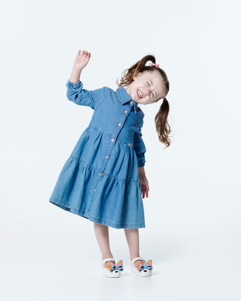 Child model in a blue dress wearing a pair of white with multi-colored patterned bow Ultragirl Wonderland baby flats
