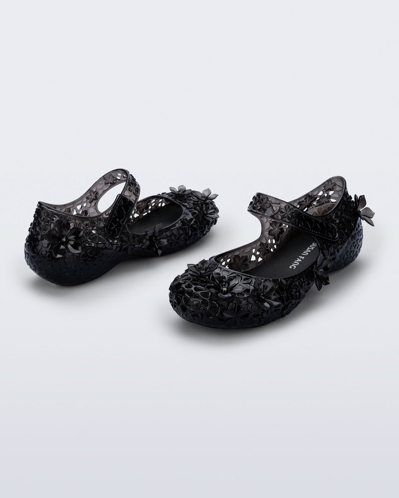 Back and side angled view of a pair of clear black Melissa + Susan Fang Luna Bloom flats with flower adornments