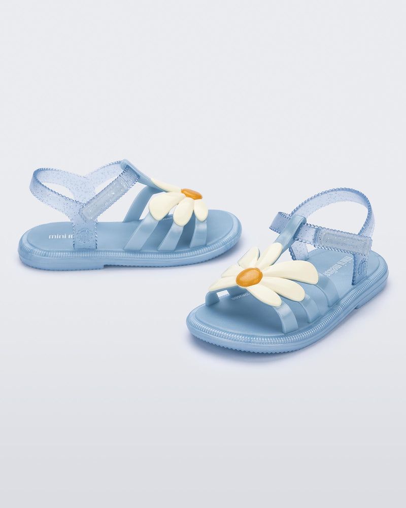 Side and angled view of a pair of metallic blue Hip Bloomy baby sandals with beige daisy on top