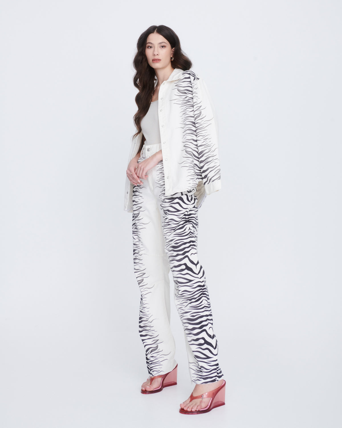 A model in a black and white pant suit wearing a pair of clear pink Nabeela heel wedge shoes