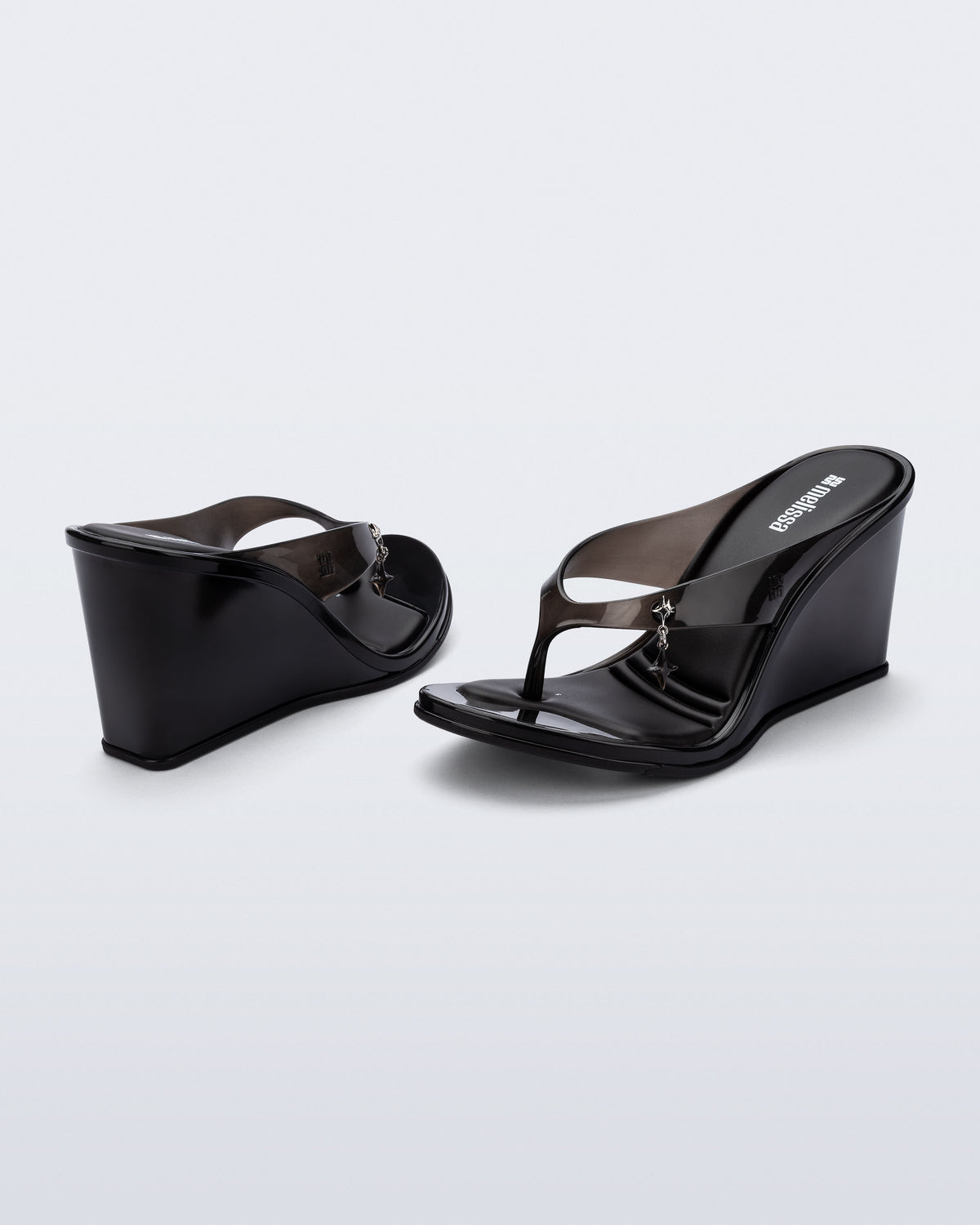 Back and angled view of a pair of black Nabeela wedge flip flops with star charm on strap