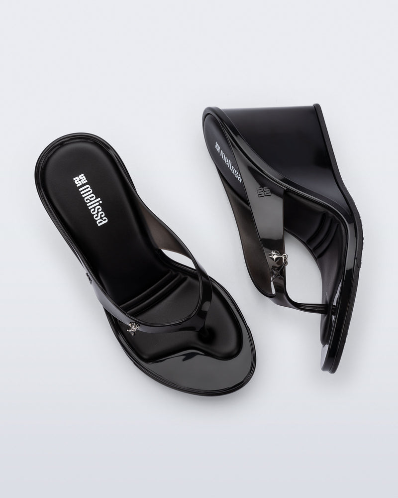 Top and side view of a pair of black Nabeela wedge flip flops with star charm on strap