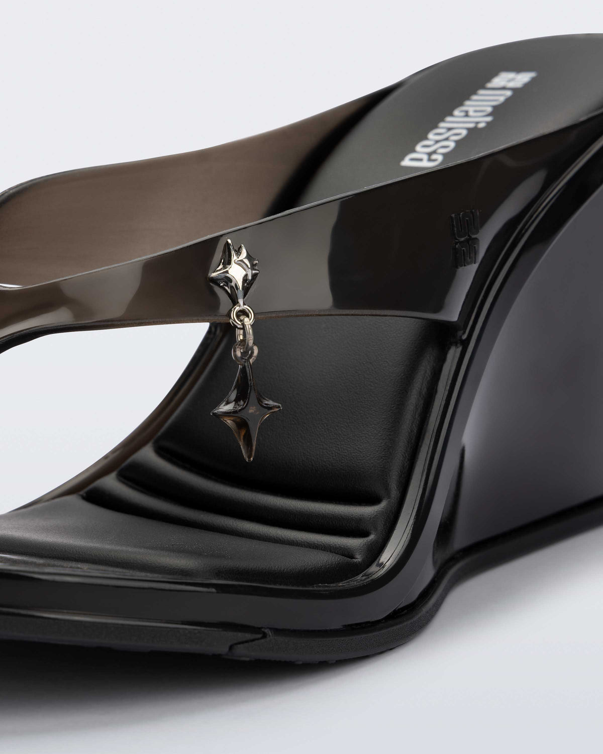 Close up of the star charm on the black Nabeela wedge flip flop.