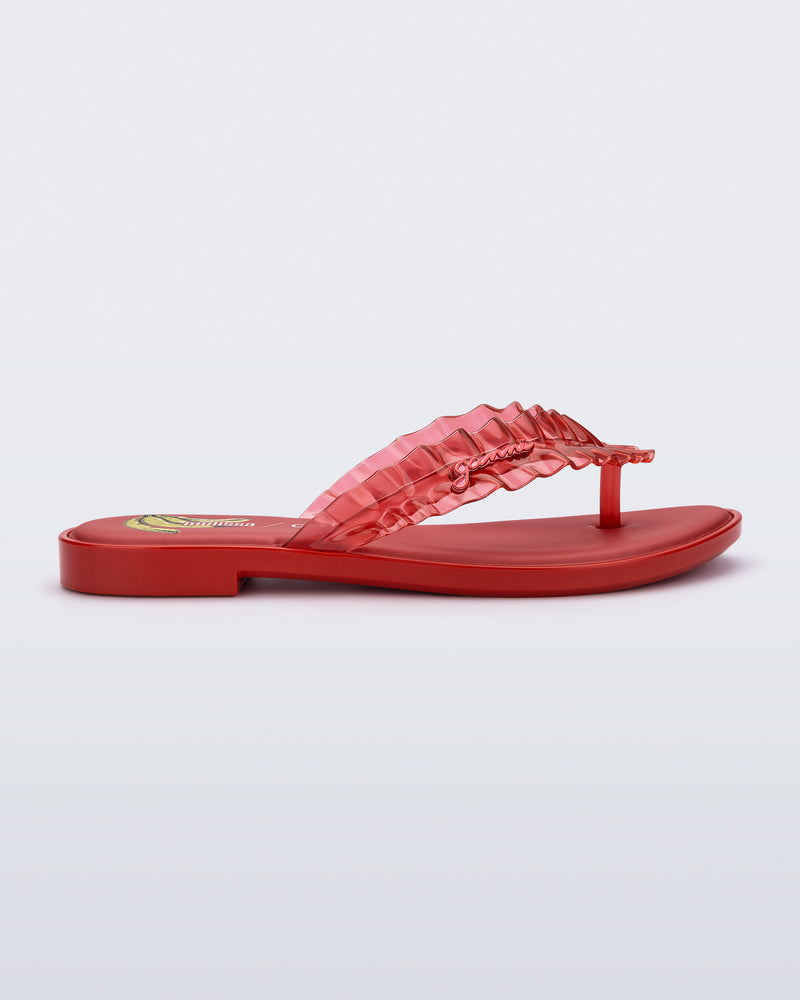 Side view of a red Flip Flop Slim + GANNI sandal with a banana print foot bed and faux ruffle strap