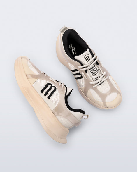 Top and side view of a pair of beige Melissa X Beat sneakers with black logo on a light gray background