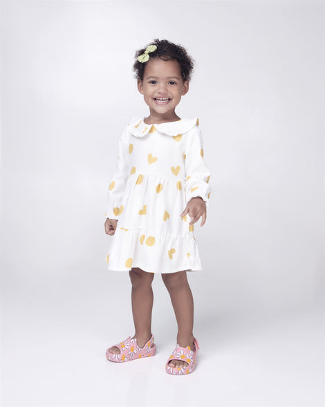 Toddler model in a white with yellow dots dress wearing a pair of pink Free Cute baby sandals with daisy print.