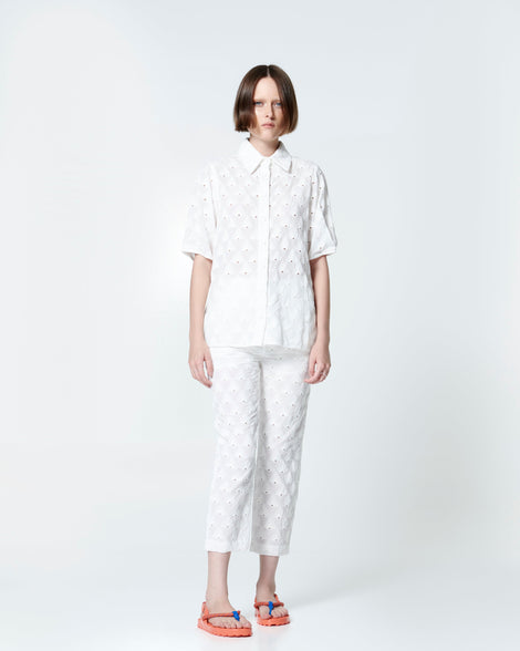 Model in a white pant set wearing a pair of orange Bond sandals with textile strap and blue toe piece