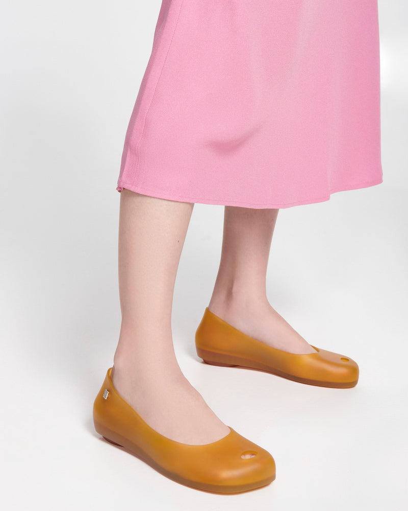 Model's legs in a pink dress wearing a pair of clear yellow Ultragirl Futura ballerina flats