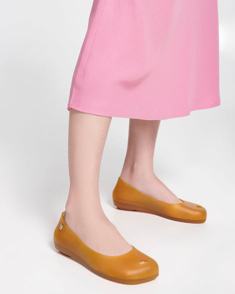 Model's legs in a pink dress wearing a pair of clear yellow Ultragirl Futura ballerina flats