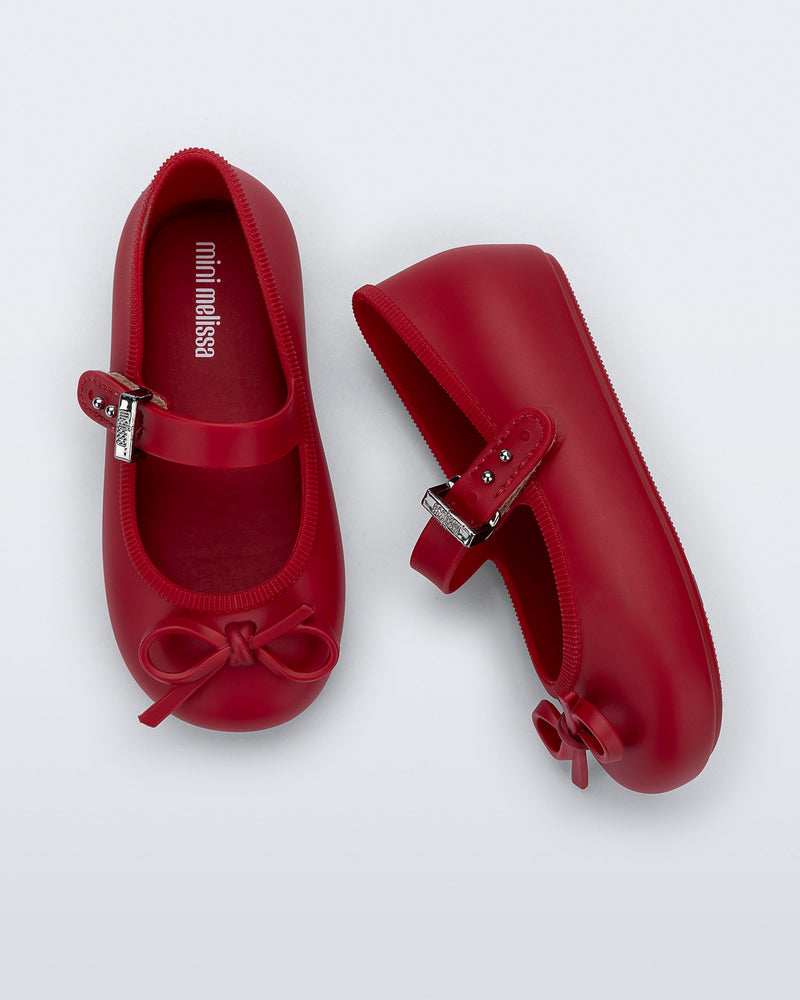Side and top view of a pair of red Soft Ballerina Delicate Bow baby flats with top strap and bow