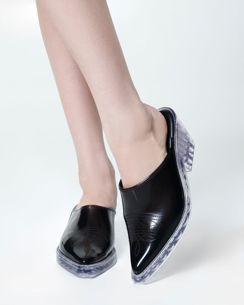 Model's legs wearing a pair of black with clear heel Texas Mule heels