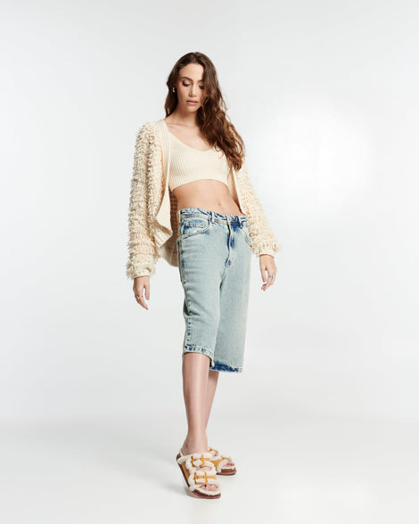 Model in long jean shorts and white top and sweater wearing a pair of orange Cozy Warm Slides with beige fuzzy insoles