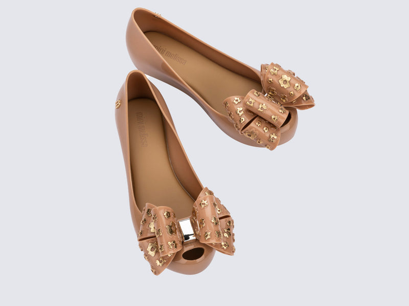 Top view of a pair of beige Ultragirl Sweet X kids flats with a bow that has chorme flowers on it