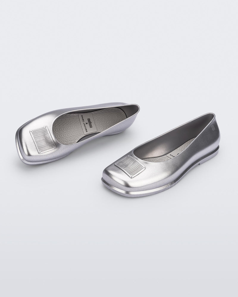 Side and angled view of a pair of metallic silver Ruby + Marc Jacobs flats