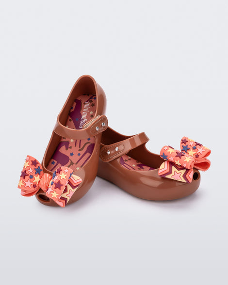 Angled view of a pair of brown with orange star patterned bow Ultragirl Wonderland baby flats