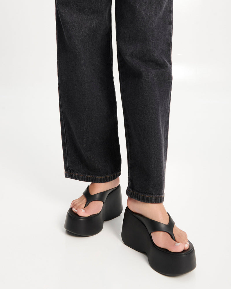 Model's legs wearing a pair of black Free Thong Wedge Platform heels