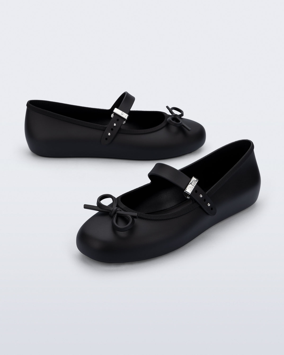 Side and angled view of a pair of black Soft Ballerina Delicate Bow flats with top strap and bow