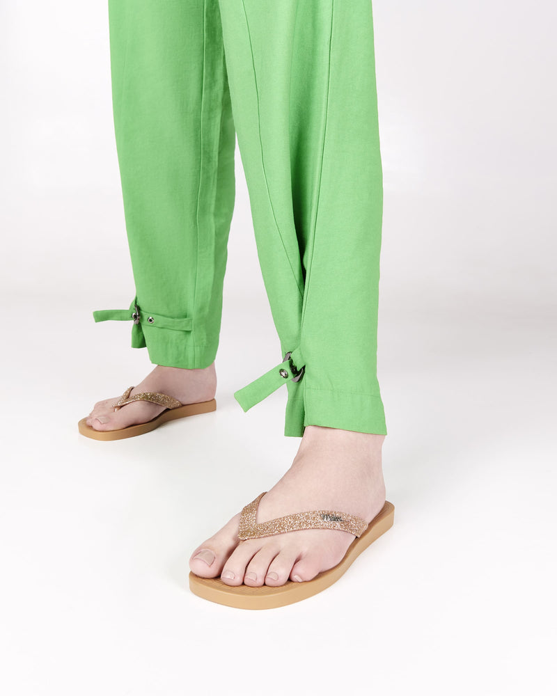 Model's legs wearing a pair of beige with brown glitter strap Sun Long Beach flip flops