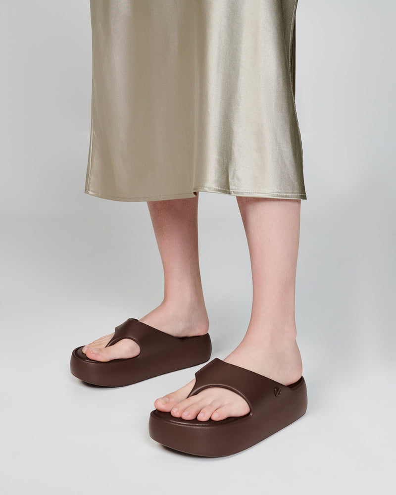 Model's legs in a beige dress wearing a pair of bronze Free Platform Thongs