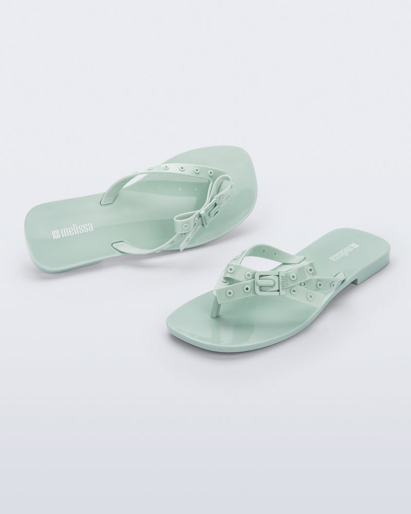 Side and angled view of a pair of green Harmonic Squared flip flops with bow on strap