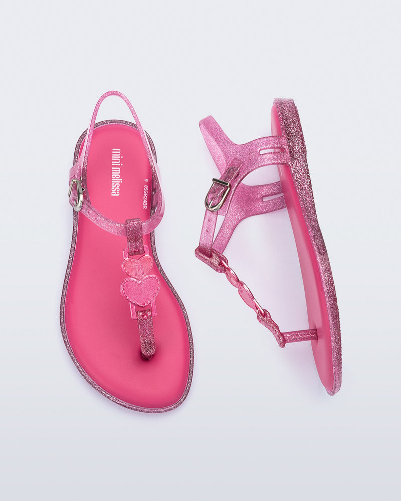 Top and side view of a pair of pink glitter Solar kids sandal with a heart embellishment