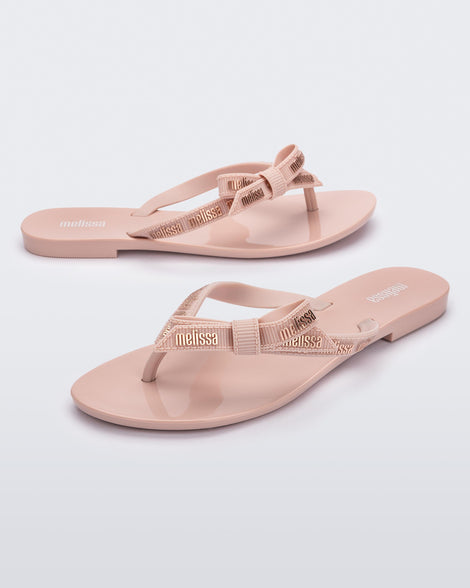 Angled view of a pair of light pink Harmonic M Lover adult flip flop with Melissa logo on strap