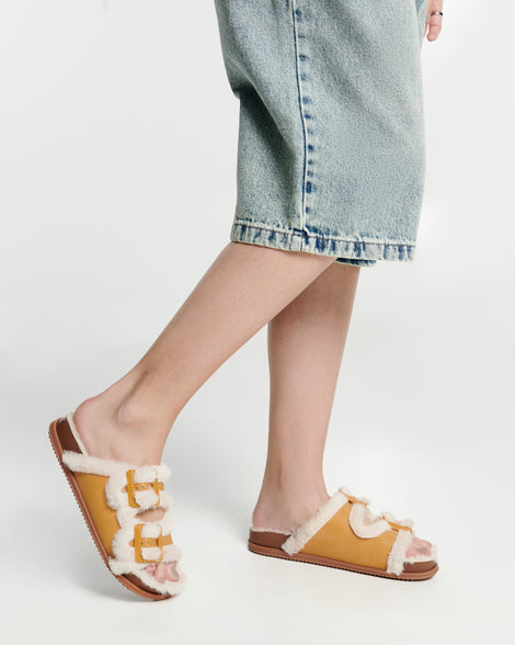 Model's legs in long jean shorts wearing a pair of orange Cozy Warm Slides with beige fuzzy insoles