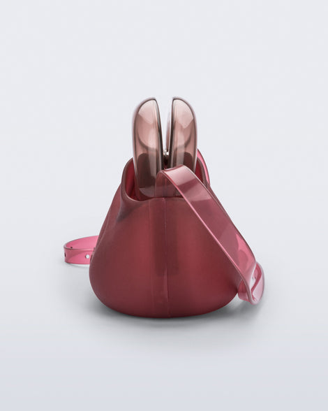 Side view of a small red bag with clear brown clutch and long strap