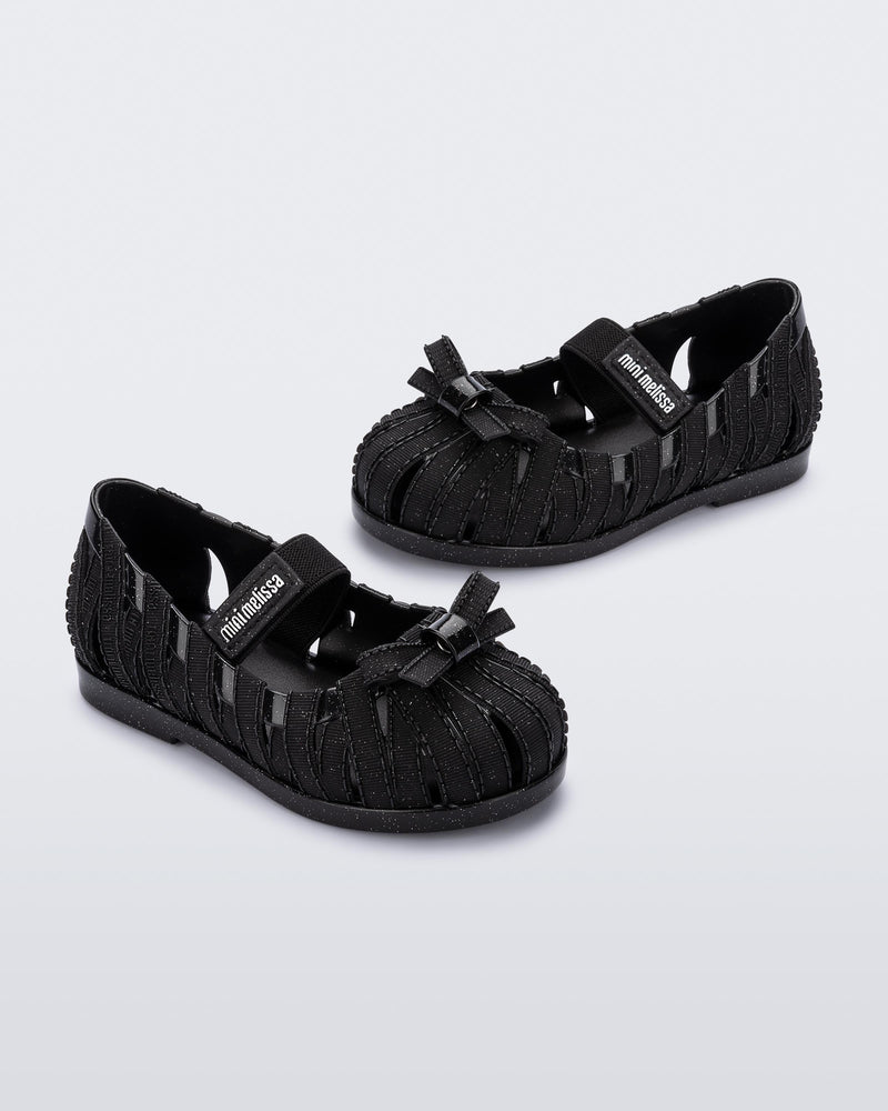 Angled view of a pair of glitter black M Lover Ballerina baby flat with bow and strap