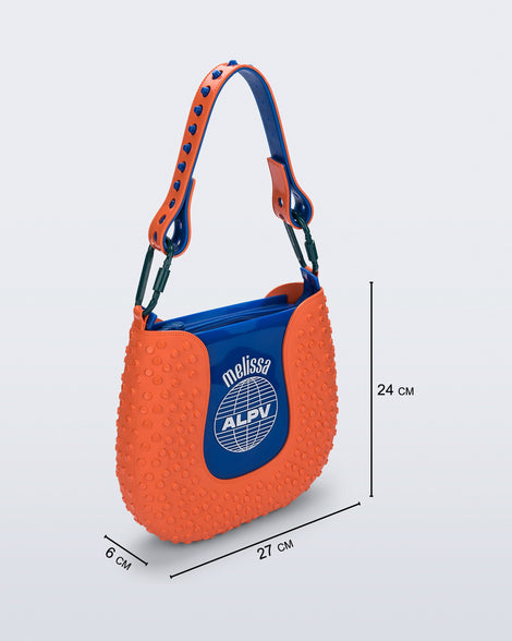 Angled view of an orange Nina Bag + Alexandre Pavao shoulder bag with blue accents with purse dimensions of 27cm x 6cm x 24cm
