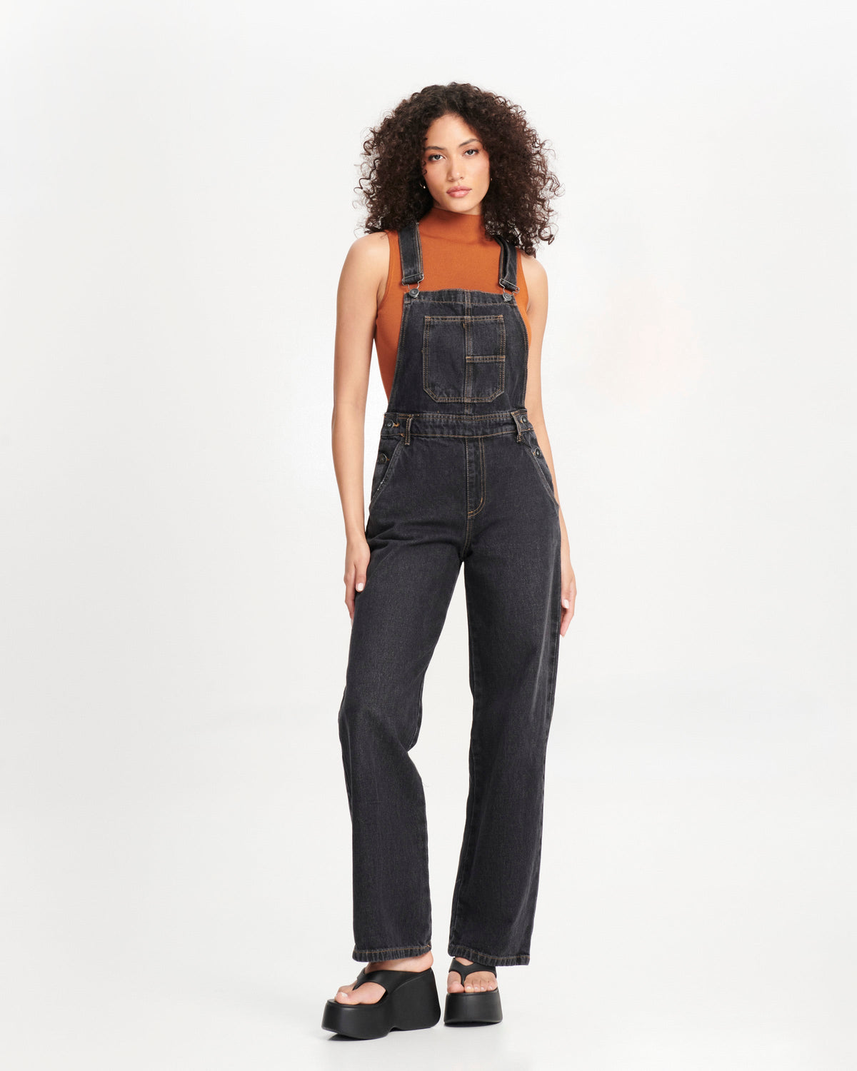Model in dark overalls wearing a pair of black Free Thong Wedge Platform heels