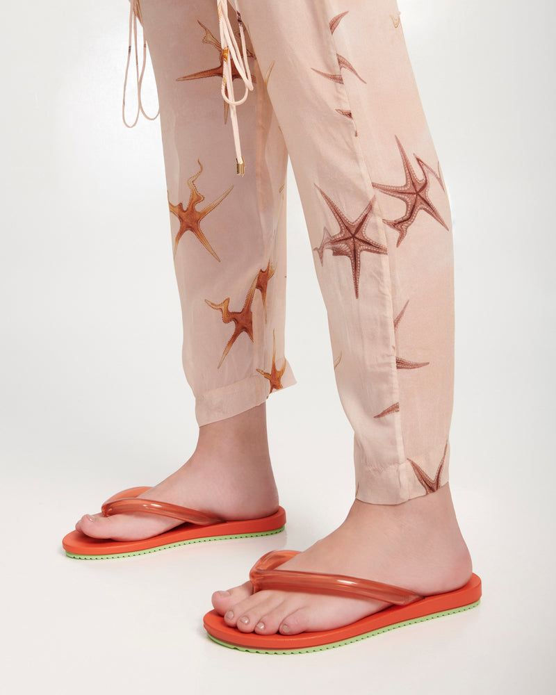 Model's legs wearing a pair of orange Flip Flop Airflow sandals with a clear orange strap and green bottom