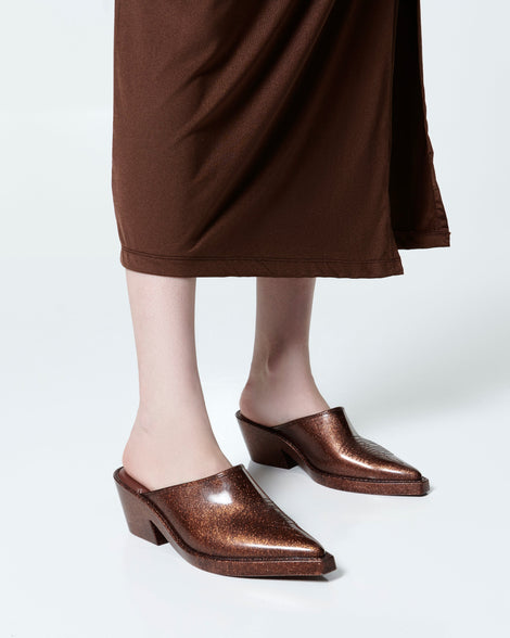 Model's legs in a brown skirt wearing a pair of bronze glitter Texas Mule heels