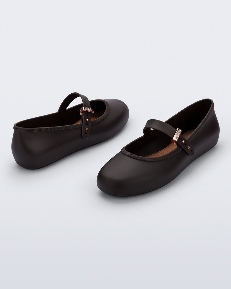 Back and angled view of a pair of brown Soft Ballerina flats with top strap and rose gold buckle