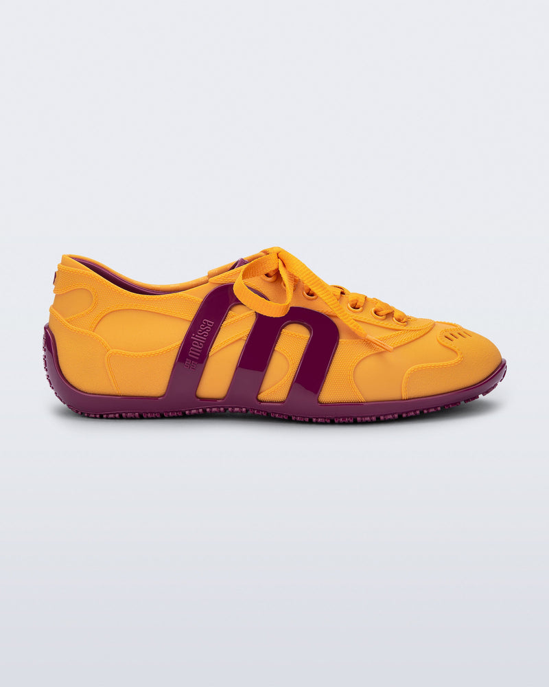 Side view of an orange-yellow Motion sneaker with pink colored sole and M monogram