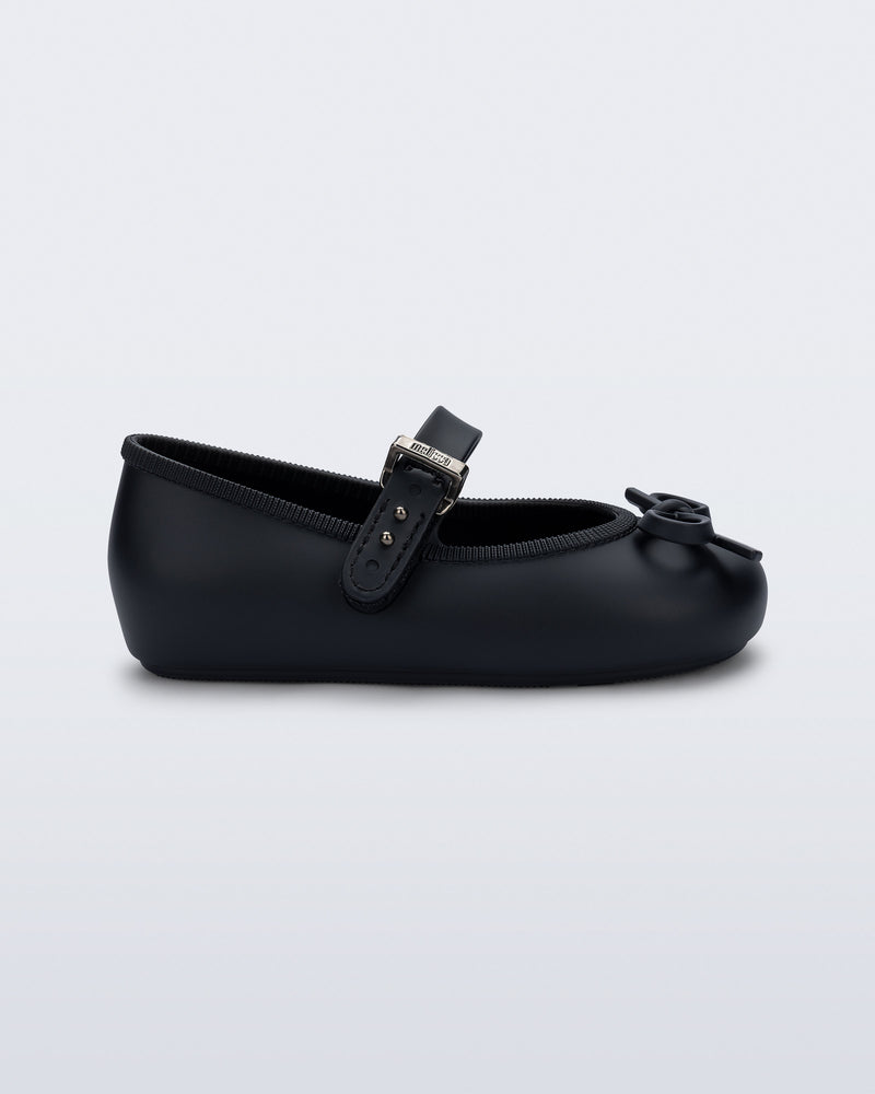 Side view of a black Soft Ballerina Delicate Bow baby flat with top strap and bow