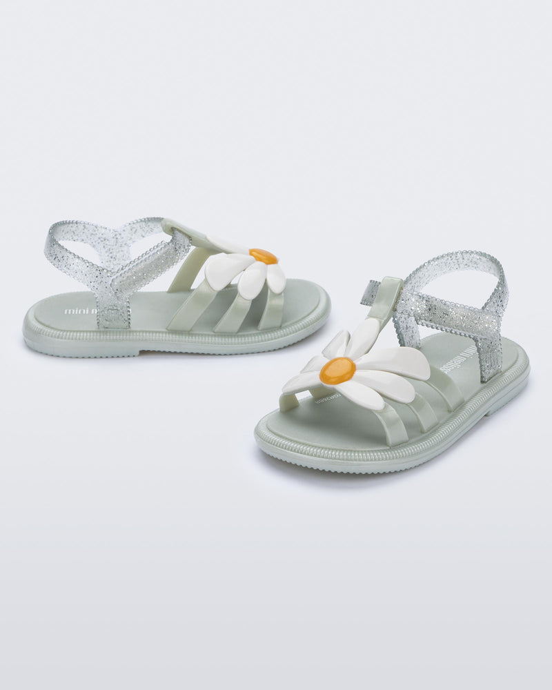 Side and angled view of a pair of metallic green Hip Bloomy baby sandals with white daisy on top