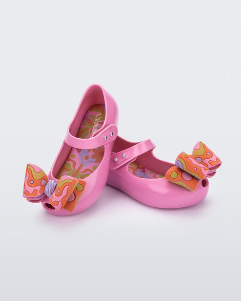 Angled view of a pair of pink with multi-colored patterned bow Ultragirl Wonderland baby flats