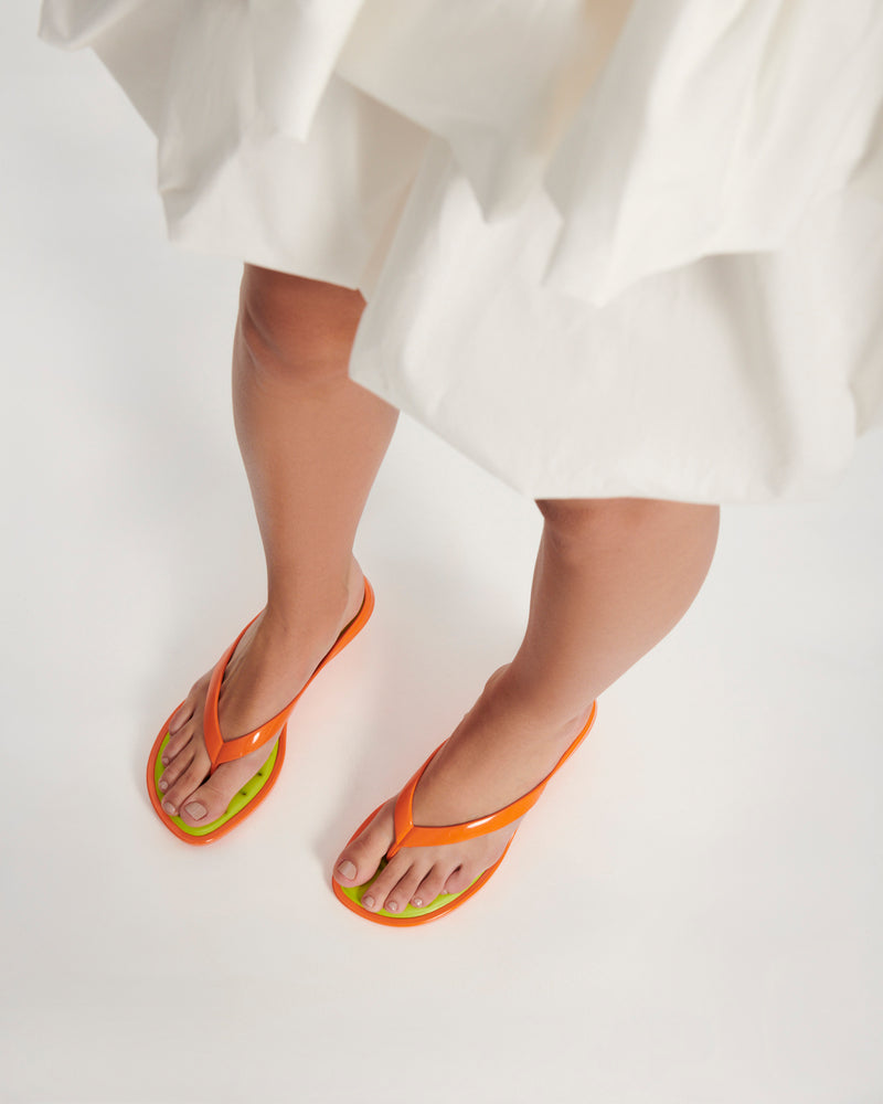 Model's legs wearing a pair of orange Flip Flop Kitten Heels with green insole