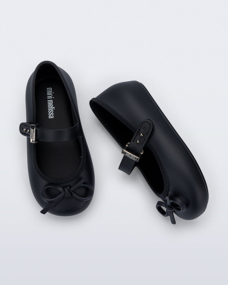 Side and top view of a pair of black Soft Ballerina Delicate Bow baby flats with top strap and bow