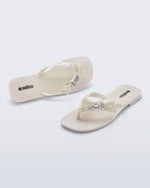 Side and angled view of a pair of beige Harmonic Squared flip flops with bow on strap