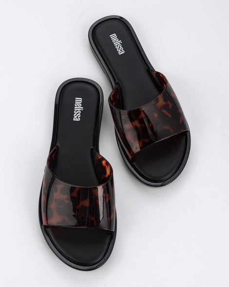 A top view of a pair of black tortoiseshell Melissa Miranda slides