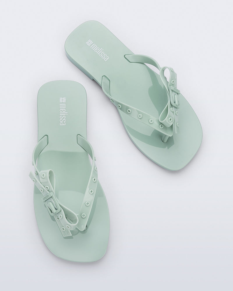 Top view of a pair of green Harmonic Squared flip flops with bow on strap