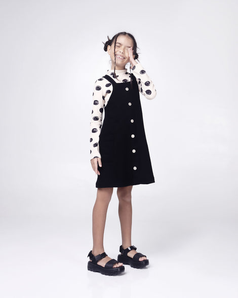 Model posing in a black jumper dress wearing a pair of Mini Melissa Kick Off platform sandals in black with adjustable velcro ankle straps